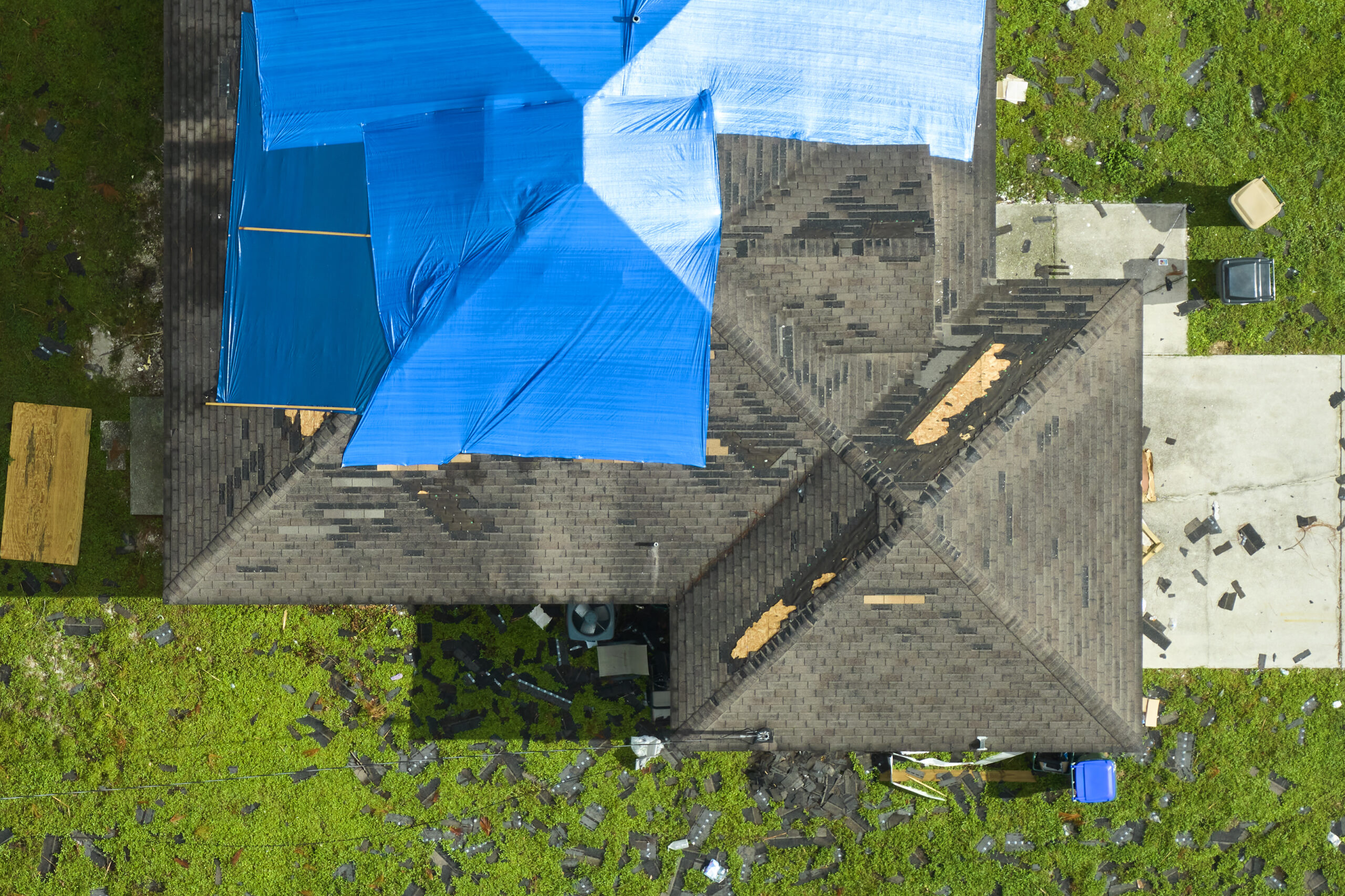 Top view of leaking house roof covered with protective tarp sheets against rain water leaks until replacement of asphalt shingles. Damage of building rooftop as aftermath of hurricane Ian in Florida